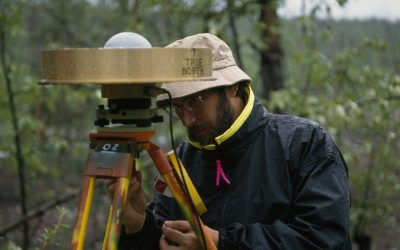 At a USGS bench mark in the woods at McCarthy, Doug Caprette of the Goddard Spa ce Flight Center removes a Global Positioning System sensor after several days of monitoring its position as part of a study of regional deformation cased by plate tectonic motion.